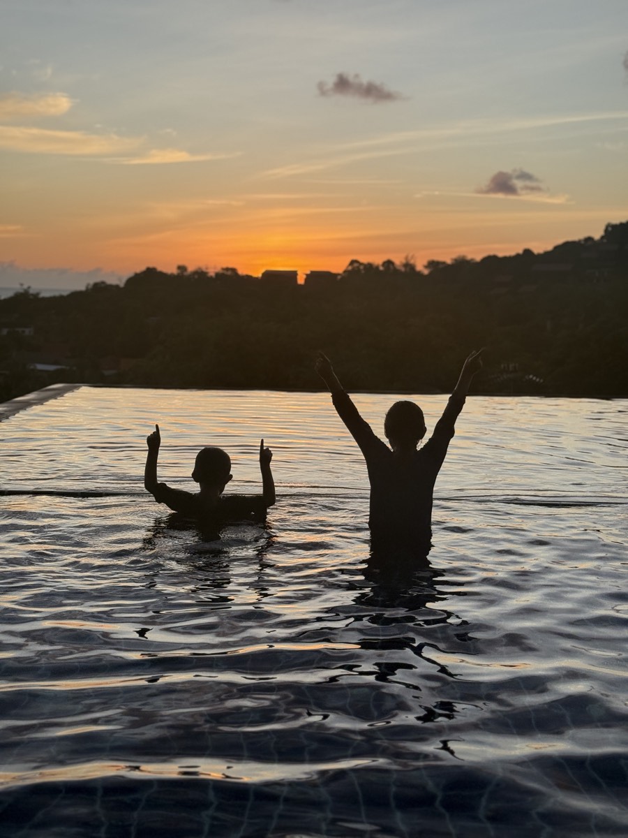 Two silhouettes in the water as the sun goes down
